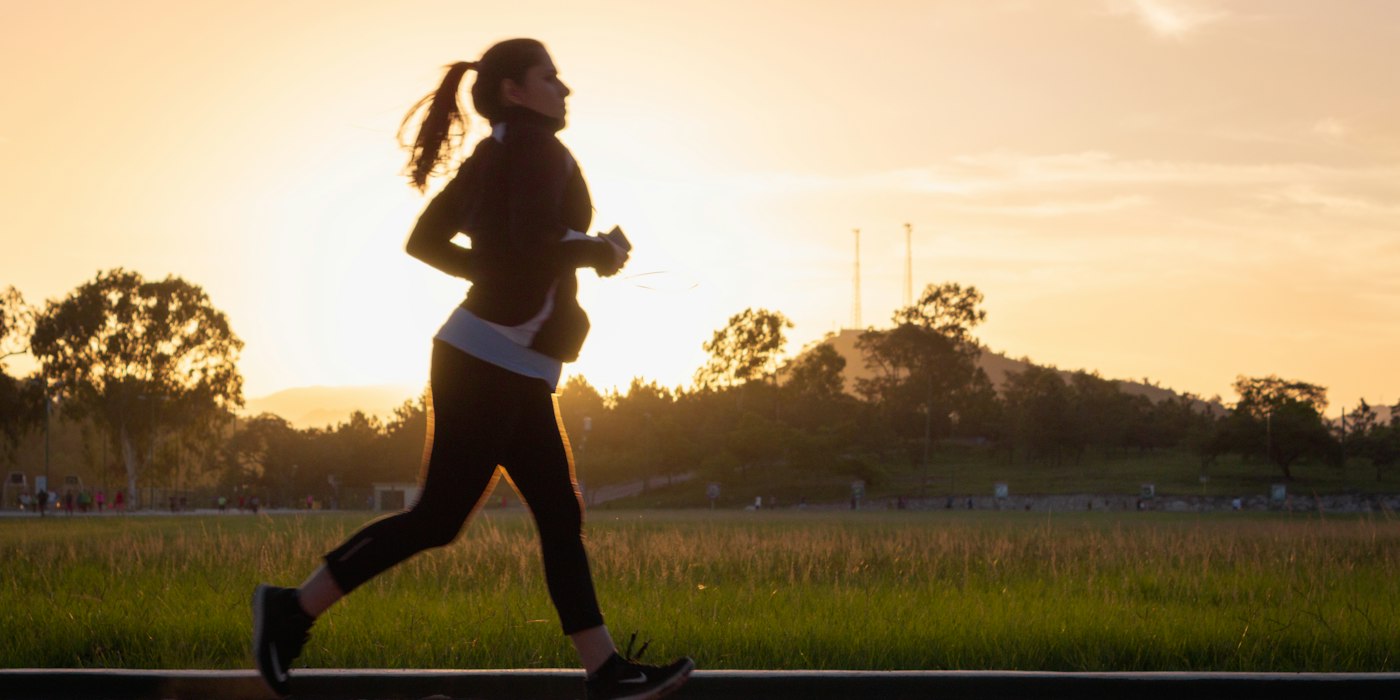 A woman running along a path at sunset, silhouetted against a golden sky