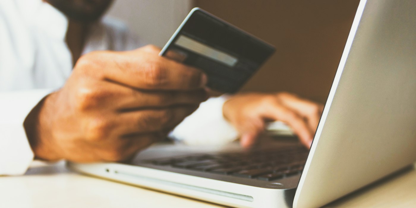 A person holding a credit card while typing on a laptop to pay for something online