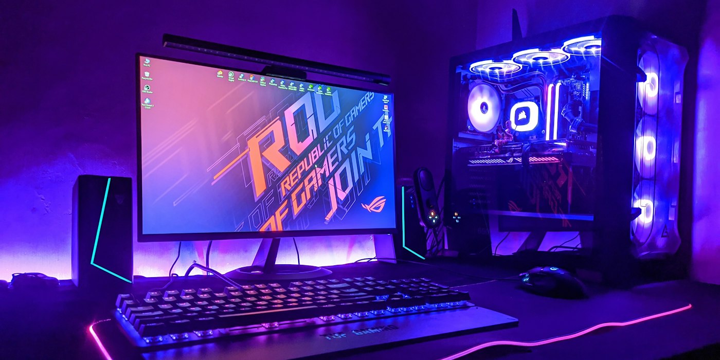 A gaming desk with a monitor, keyboard and glass-sided PC tower glowing purple