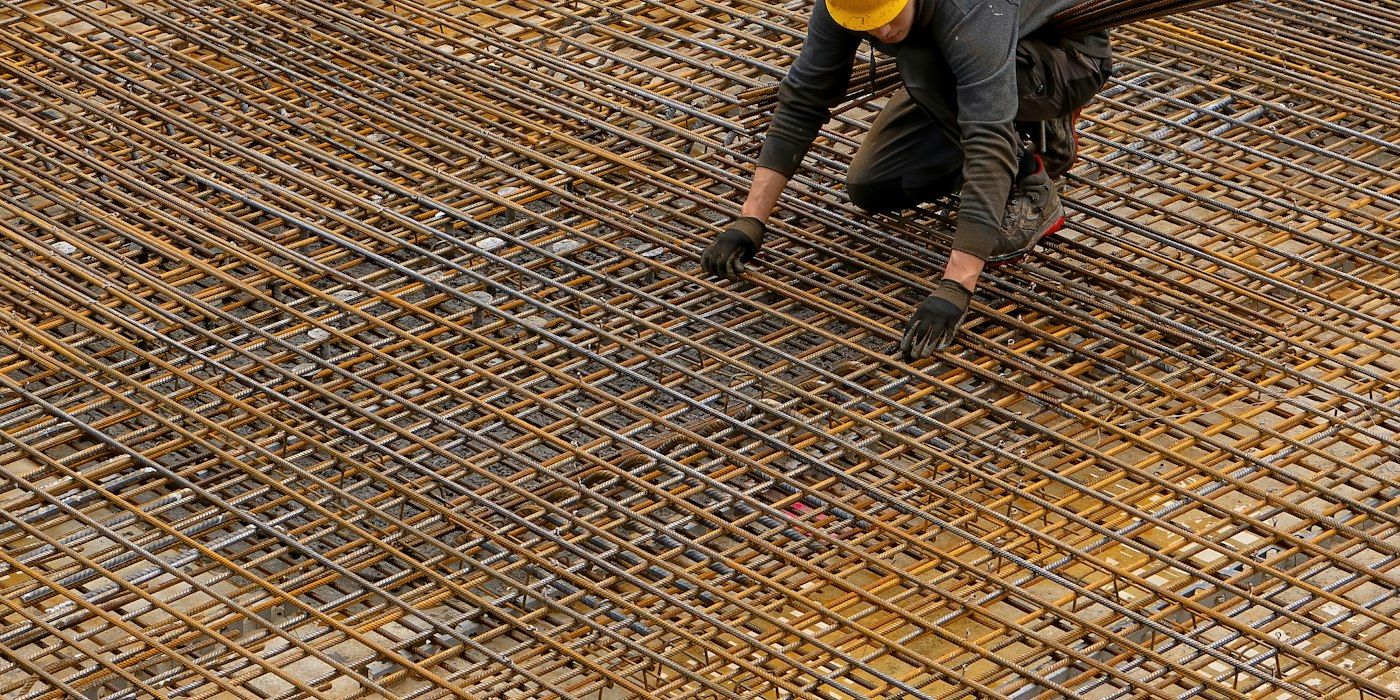 A worker in a hard hat tying steel reinforcing mesh laid out ready for a concrete pour