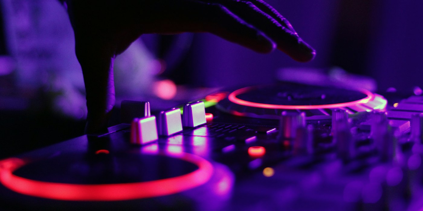 A hand resting on a DJ controller lit in purple and red light