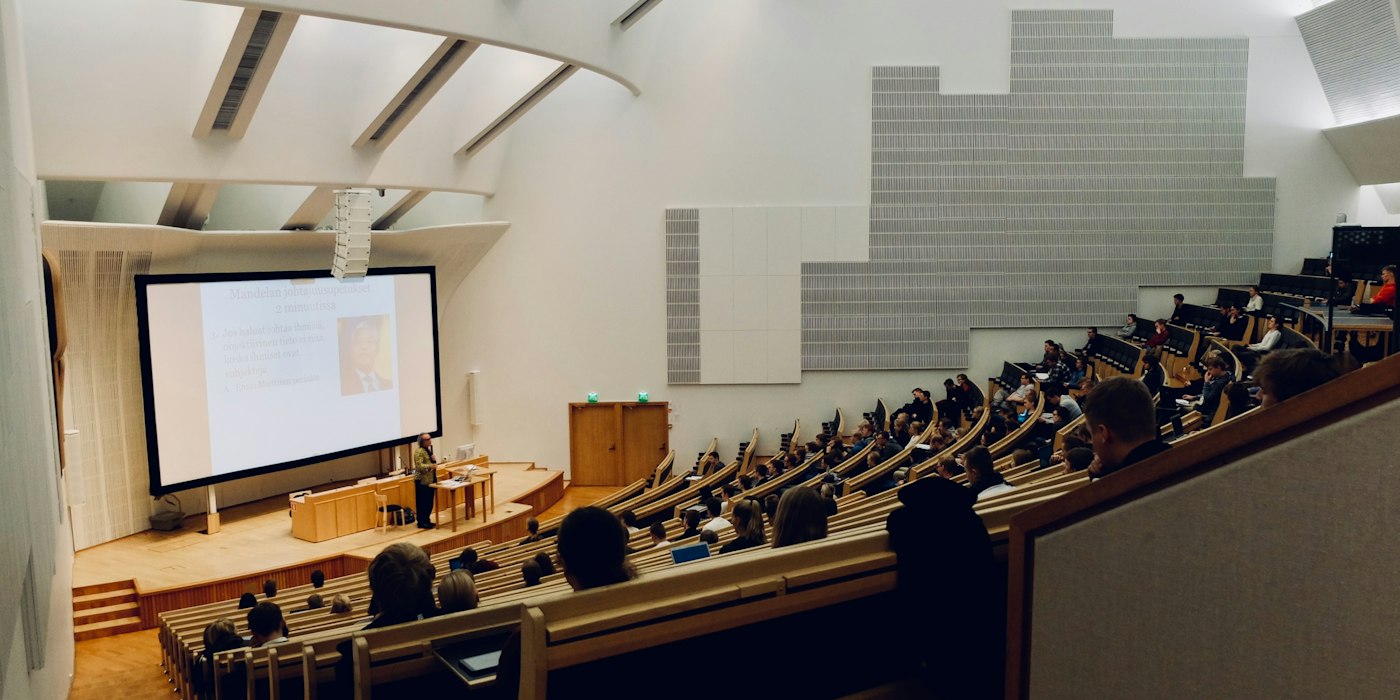 A tiered university lecture theatre full of students facing a projector screen