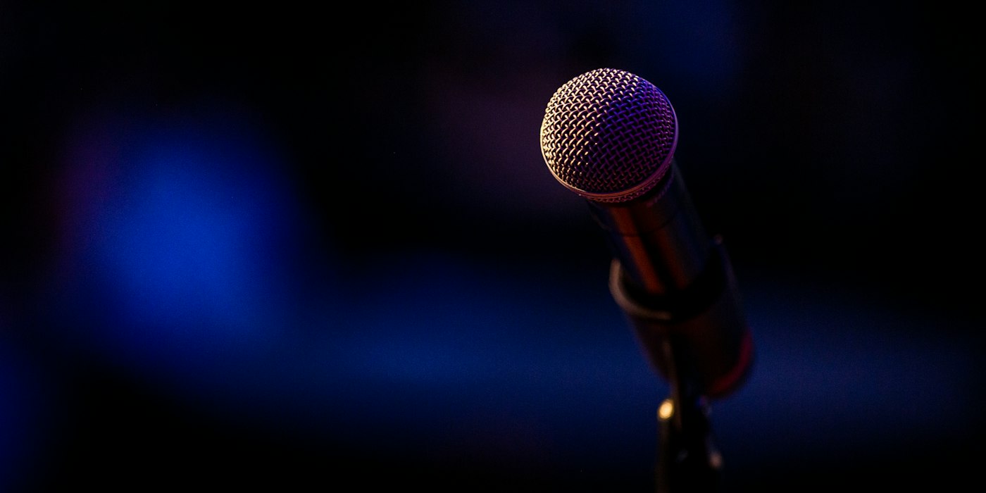 A microphone on a stand lit by a single spotlight against a dark stage