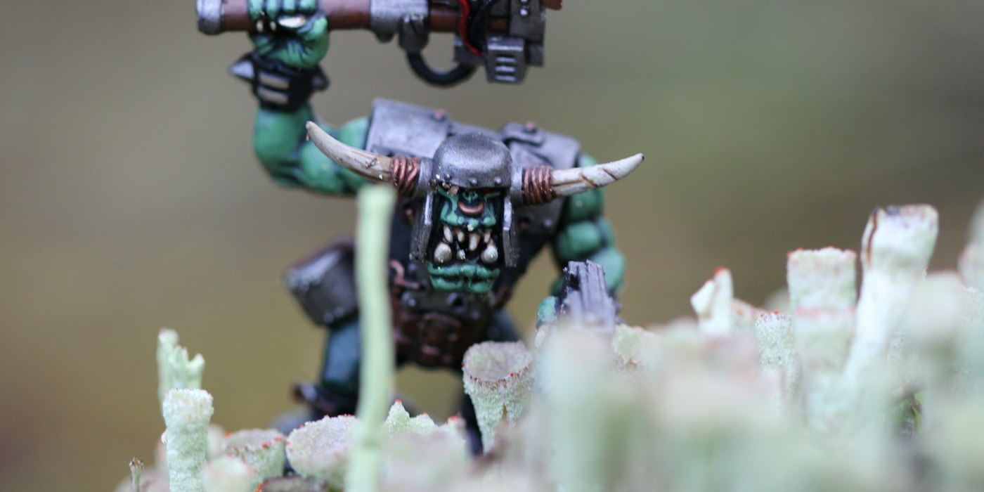 A painted orc miniature with tusks and horns standing among pale moss on a tabletop