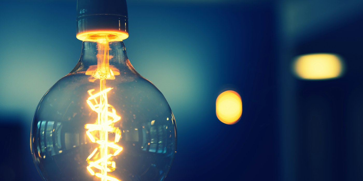 A glowing filament light bulb hanging against a dark blue background