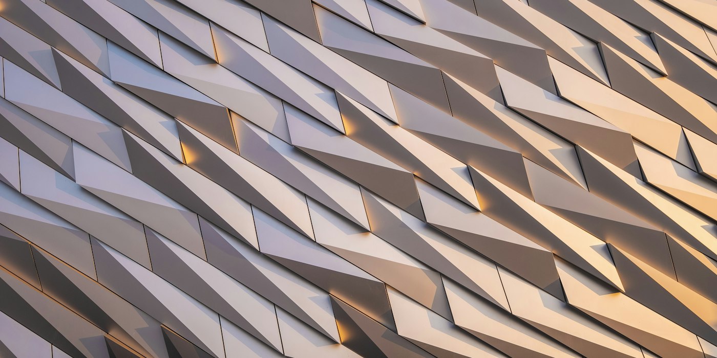 A building facade of angled metal panels catching warm light at different angles