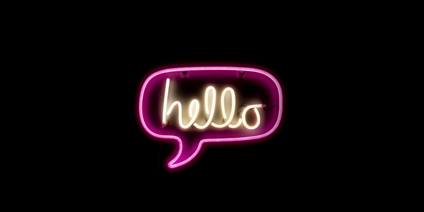 A pink neon sign spelling hello inside a speech bubble, glowing against a black wall